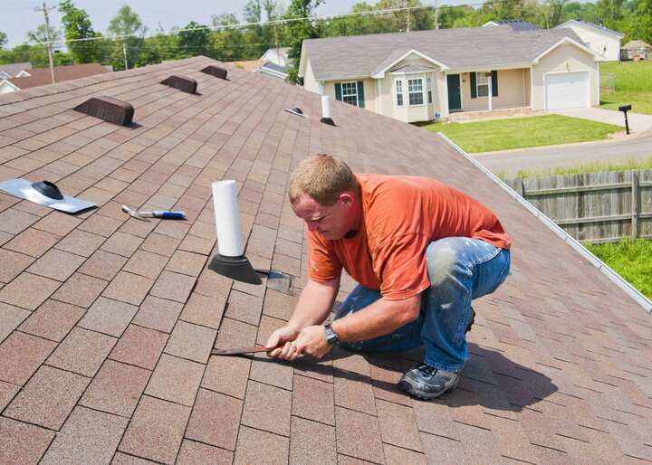 Roof and shingle repair contractor wears orange t-shirt while on roof maintenance project